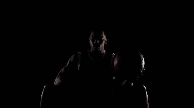 Basketball player sitting on a bench praying. Religious african american sports man against black background.
