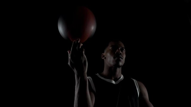 Basketball player spinning a ball. African american sports man practicing against black background.