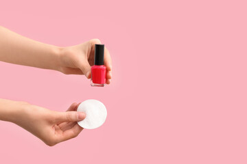 Female hands with cotton pad and nail polish bottle on pink background