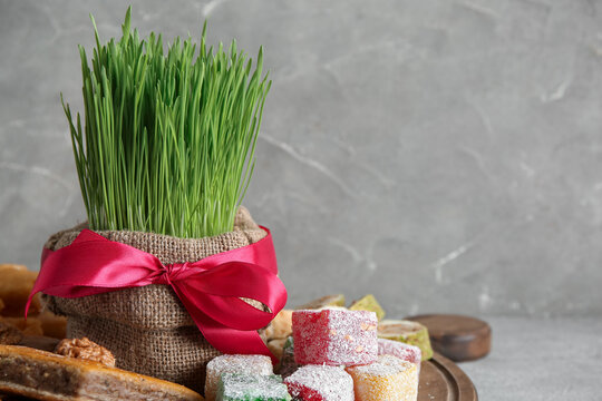 Board with green wheat grass, traditional baklava and Turkish delight on grey grunge table, closeup. Nowruz Bayram celebration