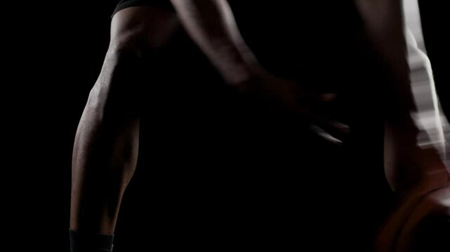Basketball player bouncing a ball. African american sports man practicing against black background. Abstract body shot front view.