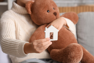 Girl with house figure and toy bear at home, closeup. Adoption concept