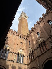 Upward view of the Torre del Mangia in Siena, Italy, framed by the Palazzo Pubblico’s brick walls. 