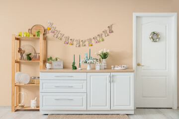 Interior of festive kitchen with flowers and Easter decorations on counter near beige wall