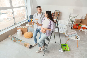 Young pregnant couple with paint roller and brush during repair in children's room