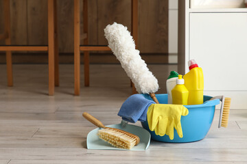 Plastic basin with cleaning supplies on floor in kitchen, closeup