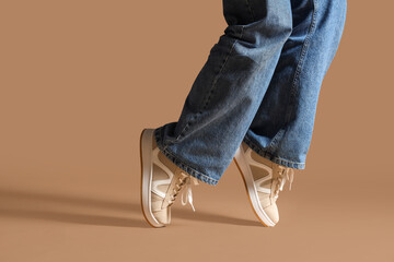 Legs of woman in stylish sneakers on beige background