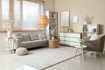 Interior of living room with sofa, armchair, shelving units and blooming branches in vases on tables