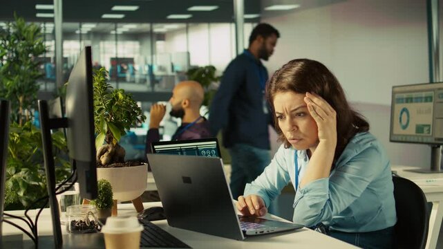 Accountant in busy modern startup agency imputing financial figures on PC after checking reports. Focused businesswoman working in modern office, crosschecking data, camera B
