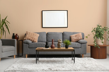 Comfortable grey sofa with soft pillows and blank photo frame hanging on beige wall in living room