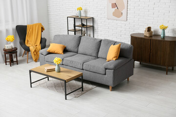 Cozy sofa with dresser, coffee table and narcissus flowers against white brick wall in living room