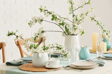 Elegant table setting with plates, glasses and blooming tree branches, closeup
