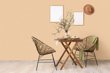 Elegant table setting with plates, glasses and blooming tree branches near beige wall