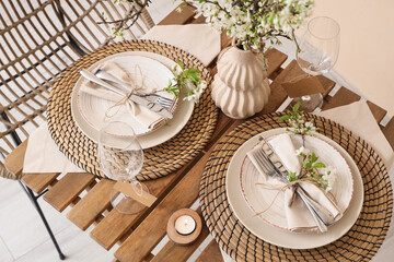 Elegant table setting with plates, burning candle and blooming tree branches, closeup
