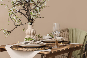 Elegant table setting with plates, burning candle and blooming tree branches