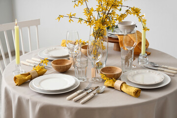 Elegant table setting with clean plates, burning candles, cutlery and blooming tree branches