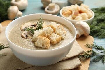 Delicious mushroom cream soup with croutons, dill and ingredients on blue table, closeup
