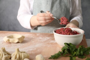 Woman making khinkali on table in kitchen, closeup