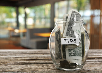 Tips jar with money on wooden table in cafe, space for text