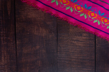 Top view of a pink Mexican tablecloth with decorations on a wooden table.