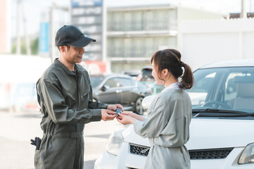 女性客から車の鍵を預かる自動車整備士の男性スタッフ
