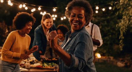Fototapeta premium Joyful african female elderly woman dancing at outdoor family gathering under lights