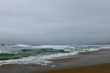 A lone seagull soars over crashing waves beneath a cloudy sky, adding motion to a dramatic coastal scene. 