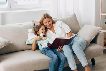 Mother and daughter enjoying quality time reading a storybook together on a cozy living room couch