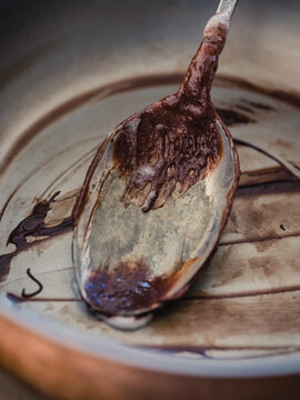 An empty bowl and spoon that has had chocolate icing  scraped out