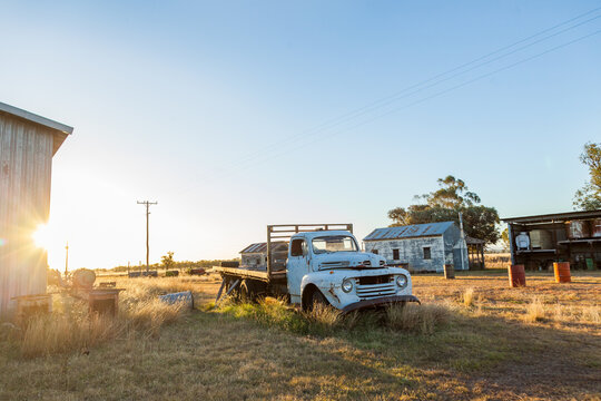 Old blue truck and other junk sitting in farm paddock at sunset