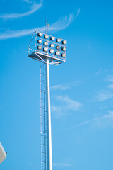 Tall metal pole with multiple stadium lights against a clear blue sky side view perspective