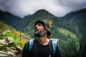 Naklejka premium Portrait of a hiker wearing a hat decorated with wildflowers, resting on a mountain trail in the Himalayas