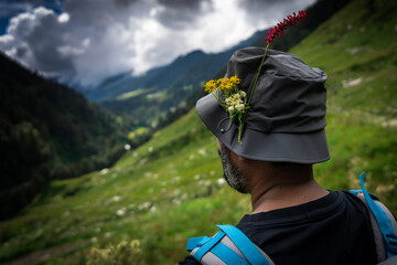 Back view of an Indian trekker wearing a flower-decorated hat, admiring the lush green landscape of...