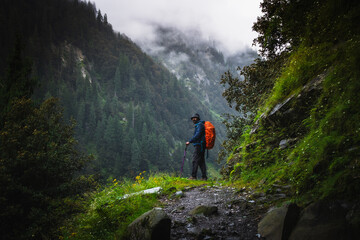 A trekker with hiking backpack on beautiful mountain landscape background. Climber hike to mountains. Hikers walking in mountain in monsoon season	