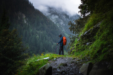 A trekker with hiking backpack on beautiful mountain landscape background. Climber hike to mountains. Hikers walking in mountain in monsoon season	