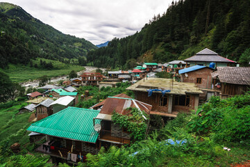 Scenic village view in Barot Valley, Himachal Pradesh, India surrounded by lush green mountains and river. © Sumit