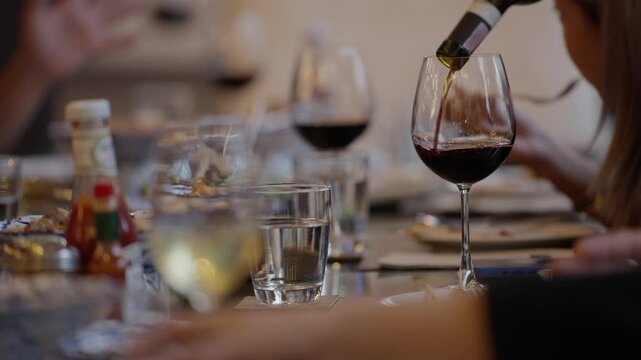A waiter is pouring red wine into a glass on a dining table at a banquet event, Waiter pouring wine for customer at hotel restaurant. Exclusive dining event, sophisticated and celebratory