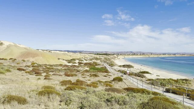 Girl in cap walks on footpath towards stunning 
Port Willunga Beach with clear water and Star of Greece shipwreck. Fleurieu Peninsula, Onkaparinga, Adelaide, South Australia