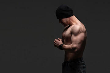 Shirtless muscular man in black beanie with hands clasped, deep in thought. Bodybuilding