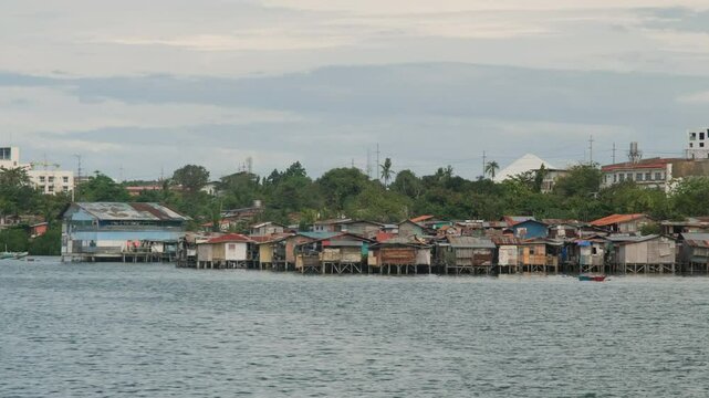 Shantytown amid tropical greenery against modern buildings on the shore of ocean in Lapu-Lapu City. Flimsy houses on piles
