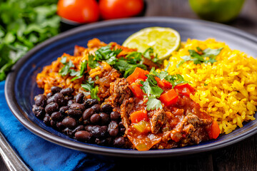 Fototapeta premium Delicious plate of vibrant Mexican food featuring rice, beans, and beef with fresh herbs and lime
