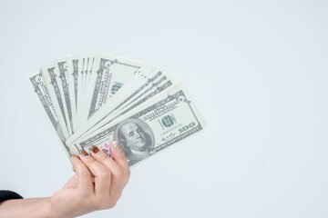Female hand holding a dollar bill fan, white background, payment concept.