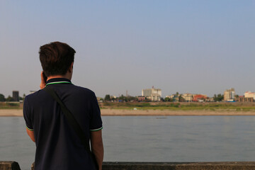 Fototapeta premium Contemplative man on riverbank city skyline photography urban environment rear view reflection on life