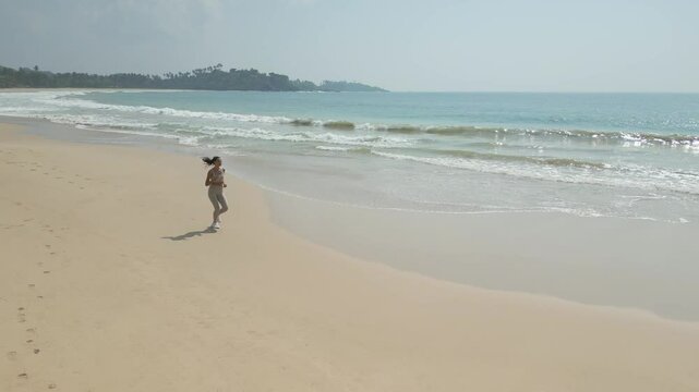 Cinematic drone view of athletic woman jogging on pristine sandy beach in Sri Lanka. Perfect for health, sporty lifestyle, holiday, or solo female travel promotional videos.