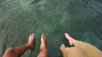 two pairs of legs hanging above the clear sea water, suitable for holiday, nature and couple theme...