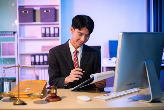 Young Asian lawyer at desk with legal scales and gavel, writing documents in office, offering legal services