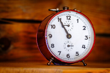 Vintage red alarm clock sitting on a wooden surface showcasing intricate clock face and aged design...