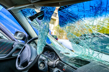Damaged blue car with shattered windshield in a junkyard during daylight hours showcasing rust and...