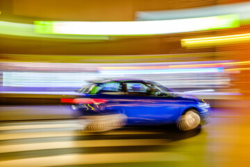 Motion blur captures a black vehicle speeding through a city street illuminated by festive lights...