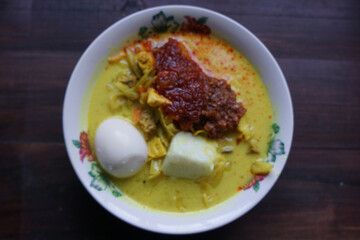 Lontong, a traditional Southeast Asian dish of compressed rice cakes in rich coconut curry, served with lodeh, sambal kacang, sambal tumis, hard-boiled eggs, and fresh vegetables on a decorative plate